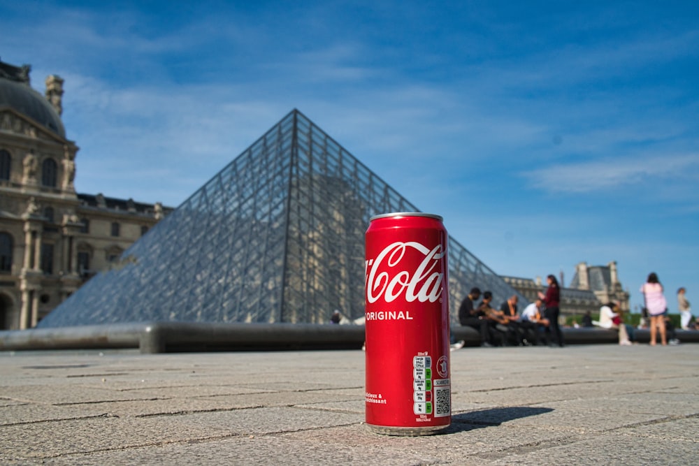 a can of coca - cola sitting on the ground in front of a pyramid