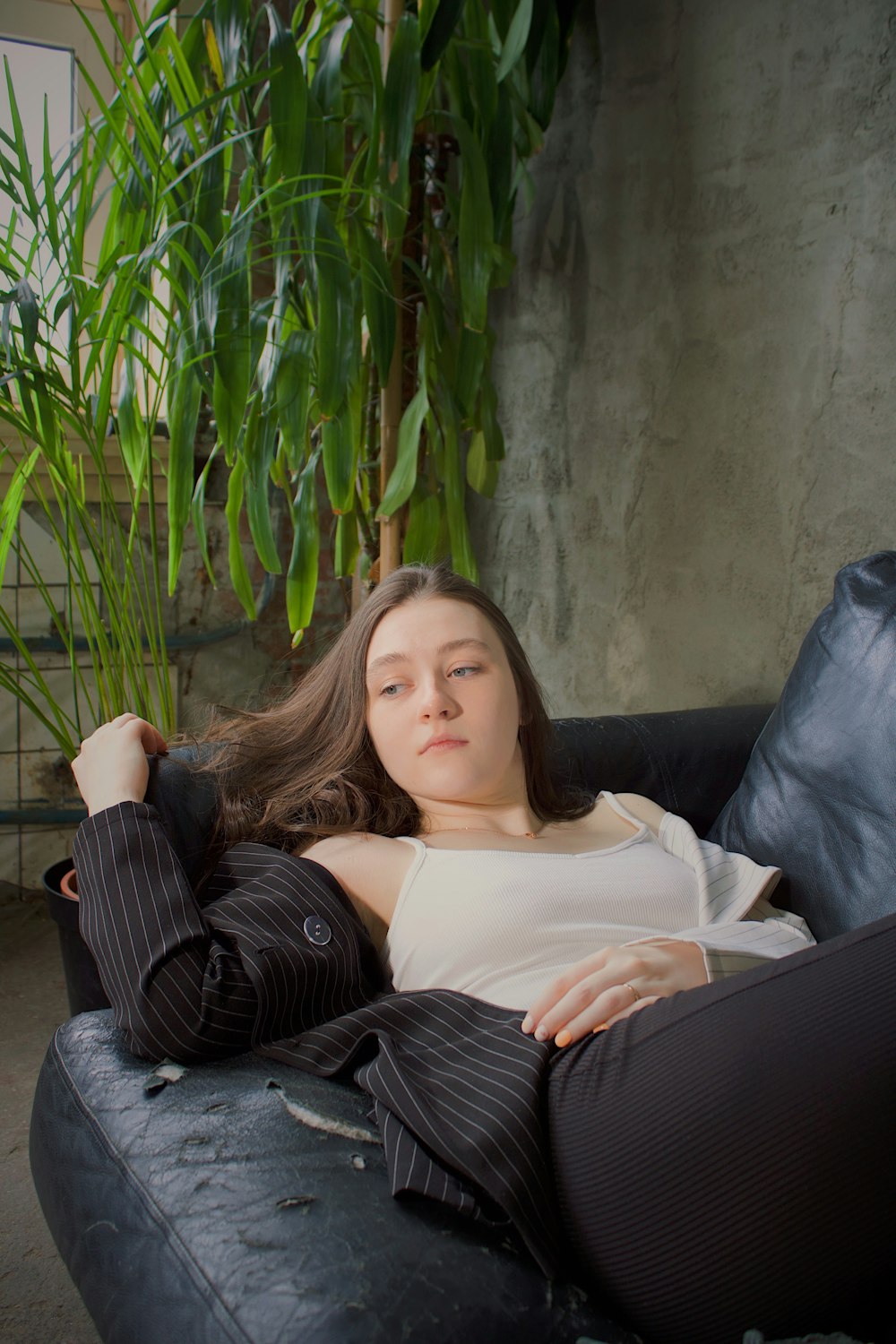 a woman laying on top of a couch next to a plant