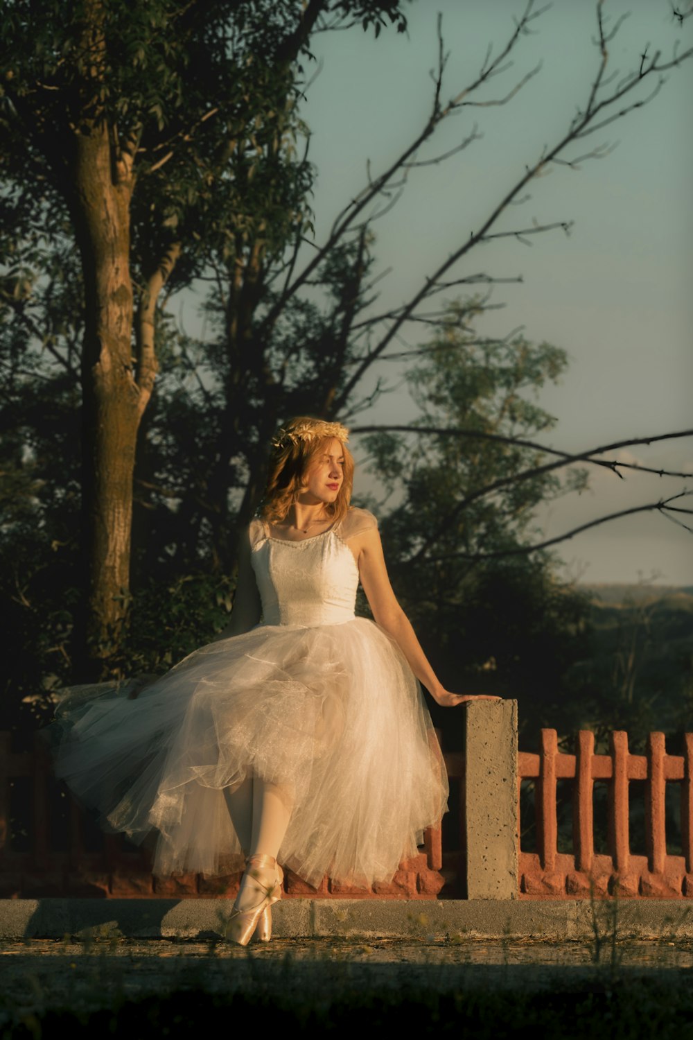 a woman in a white dress is sitting on a fence