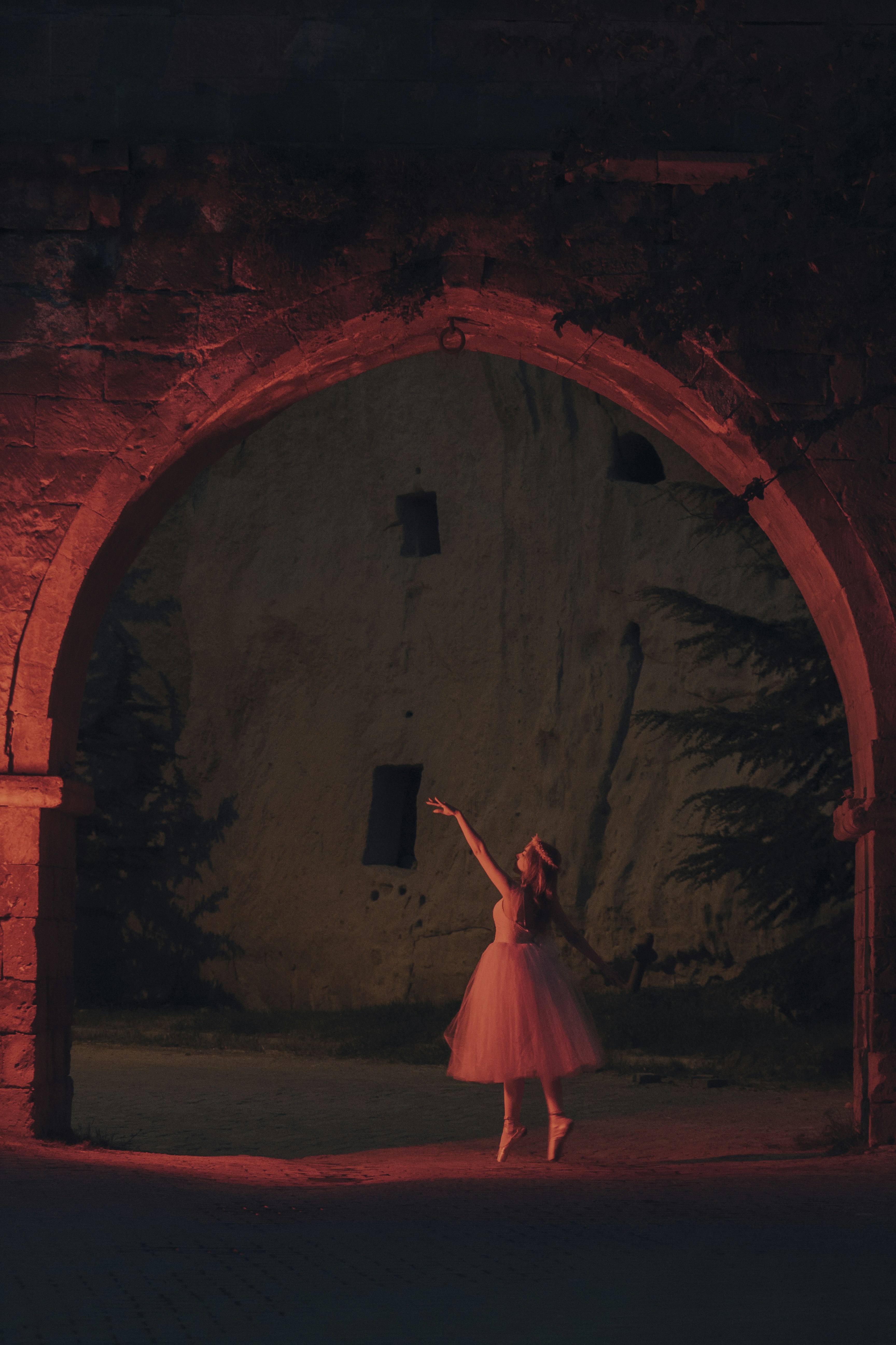 a woman in a pink dress standing in front of a stone arch