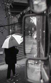 Black and white street photography capturing a candid moment of a person walking under an umbrella.
