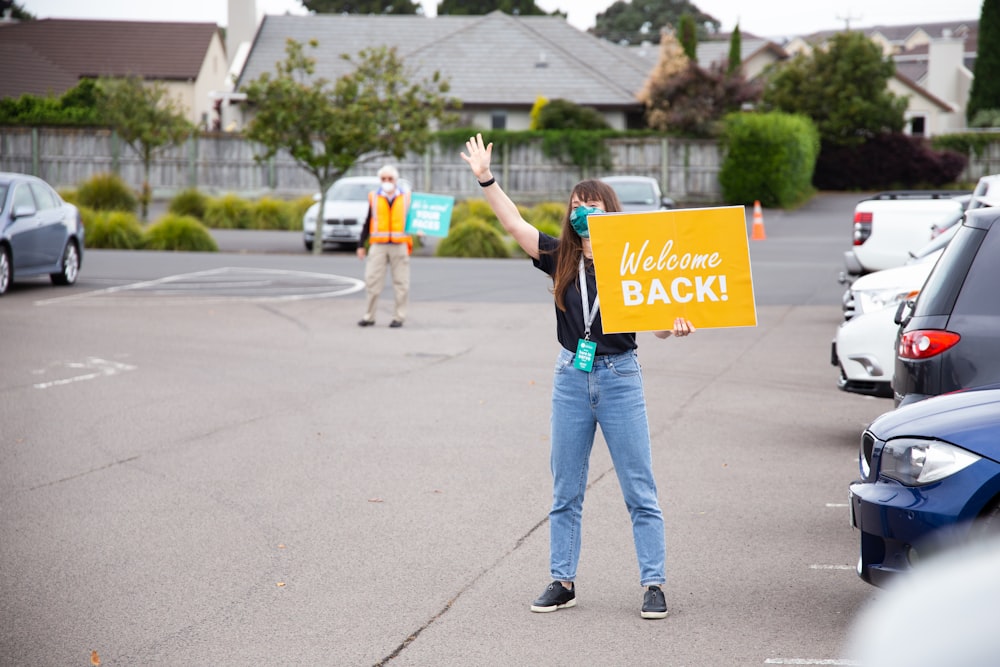 a woman holding a welcome back sign in a parking lot