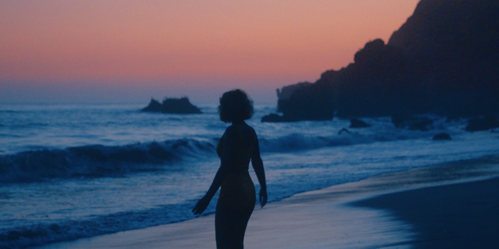 a woman walking on the beach at sunset