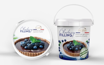 A pair of containers with blueberry filling. The front lid displays an image of a tart topped with blueberries and blackberries, garnished with mint leaves. The brand name 'Fil d'OR' is visible, promoting sustainable agriculture and quality. The larger bucket offers a similar design with additional text highlighting 'all natural ingredients' and the net weight of 6kg (13.4 lbs).