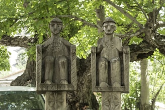 a couple of statues sitting next to a tree