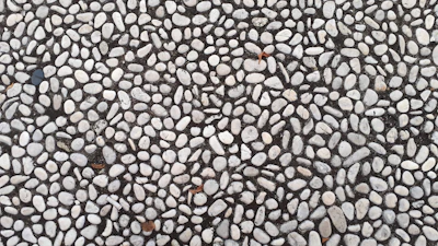 Hands spreading resin over a bed of small stones during the stone carpet installation process.