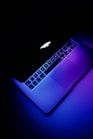 an apple laptop with a glowing keyboard on a dark surface