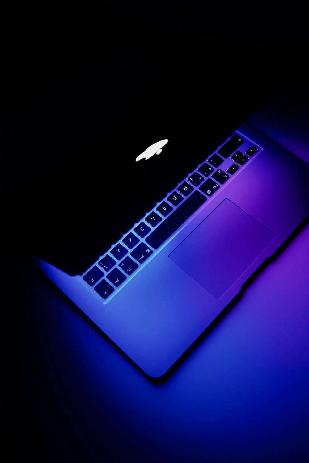 an apple laptop with a glowing keyboard on a dark surface