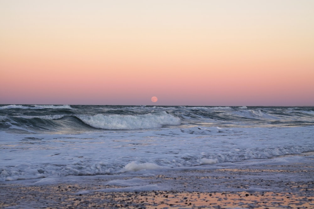 the sun is setting over the ocean waves