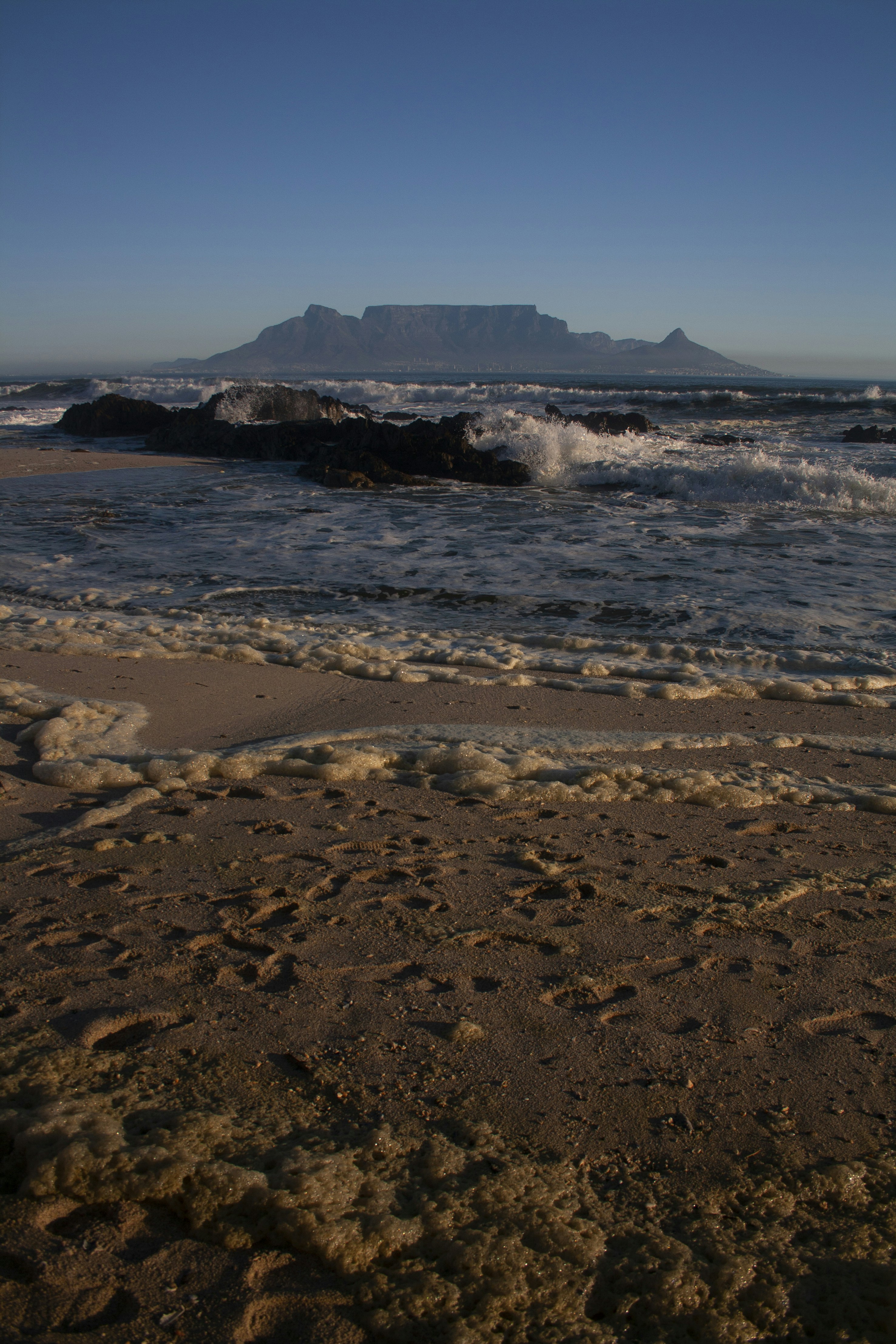 a sandy beach with waves coming in and a mountain in the distance