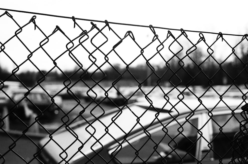 a black and white photo of cars behind a chain link fence