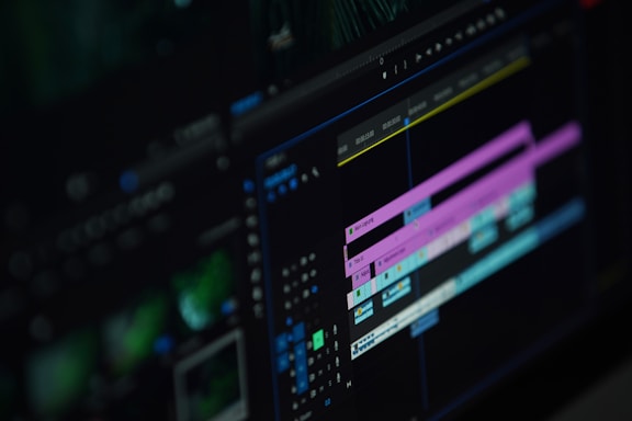 A close-up of a computer screen displaying a video editing software interface with multiple timeline tracks in purple and blue, knobs, and various editing tools visible.