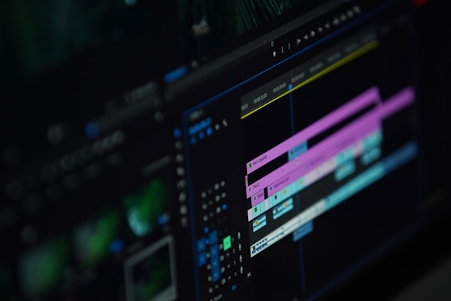 A close-up of a computer screen displaying a video editing software interface with multiple timeline tracks in purple and blue, knobs, and various editing tools visible.
