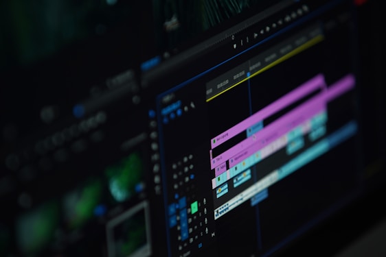 A close-up of a computer screen displaying a video editing software interface with multiple timeline tracks in purple and blue, knobs, and various editing tools visible.