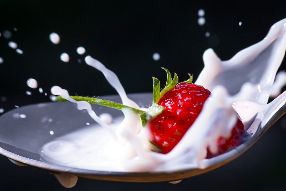 a strawberry being dropped into a bowl of milk