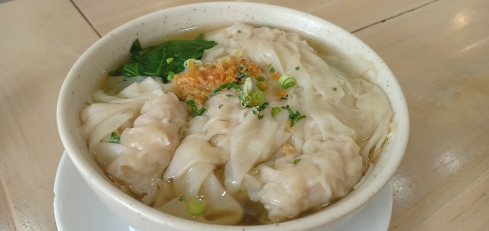 a white bowl filled with dumplings on top of a wooden table