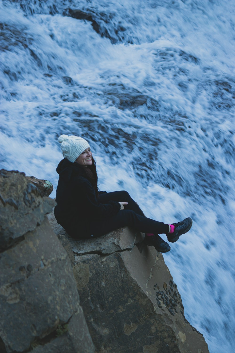 a man sitting on top of a rock next to a body of water