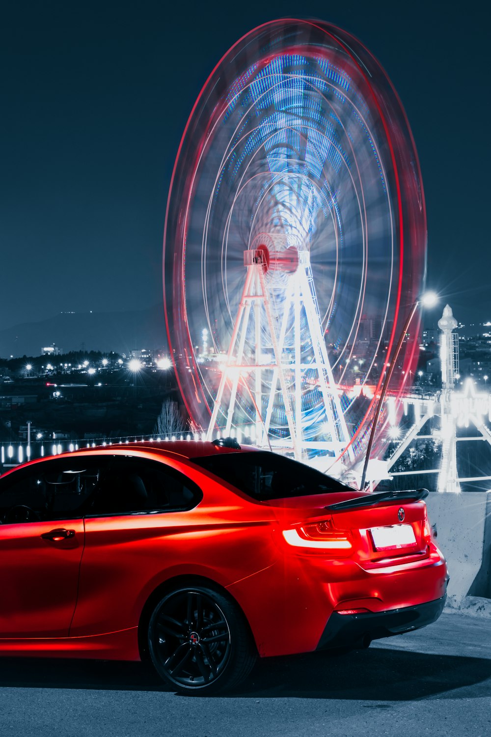 Un coche rojo aparcado delante de una noria