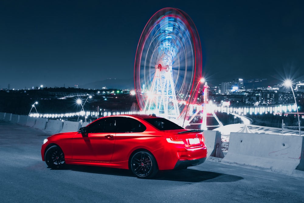 Un coche rojo aparcado delante de una noria