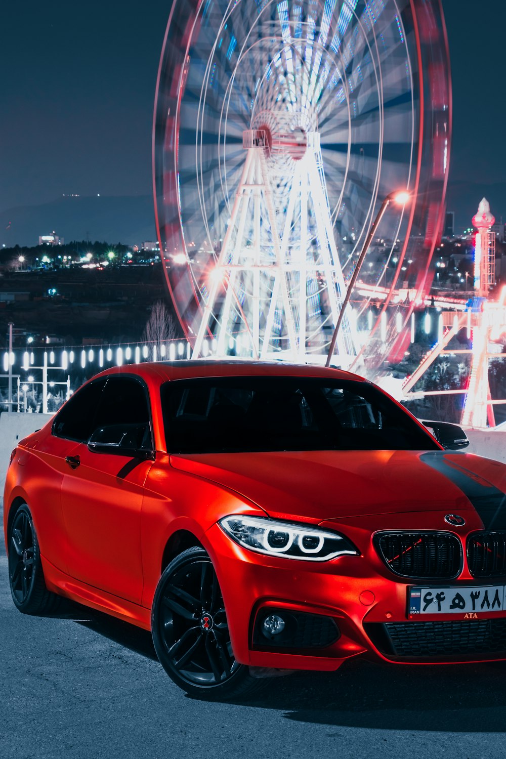 a red car parked in front of a ferris wheel