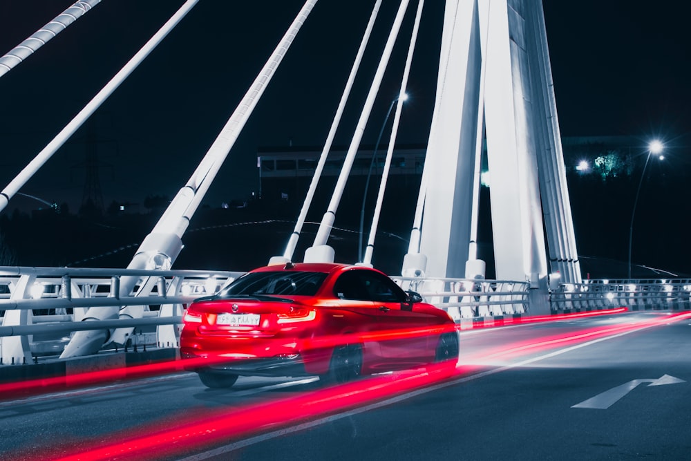 a red car driving across a bridge at night