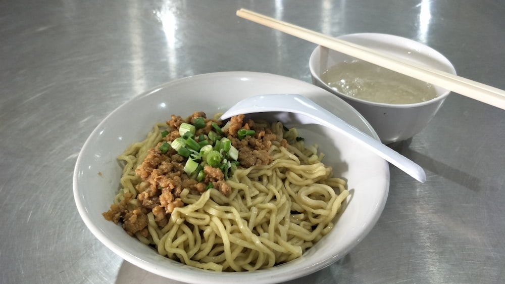 a bowl of noodles with meat and vegetables with chopsticks