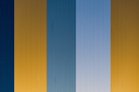 Vertical corrugated metal panels are arranged in an alternating pattern of blue and yellow hues. The surface features a repetitive texture with ridges running vertically.