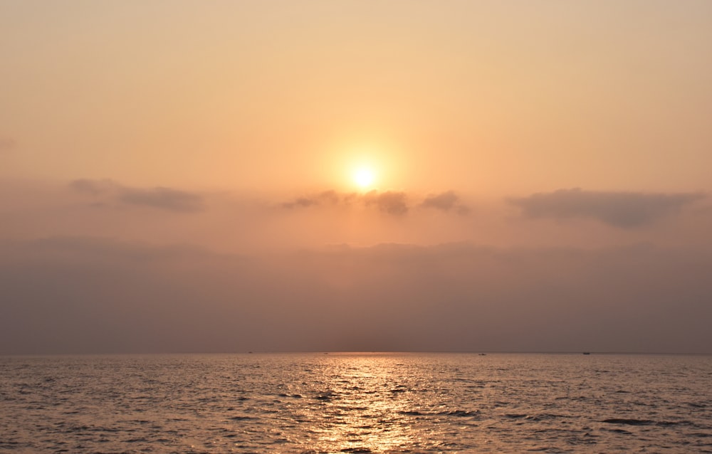 the sun is setting over the ocean on a cloudy day