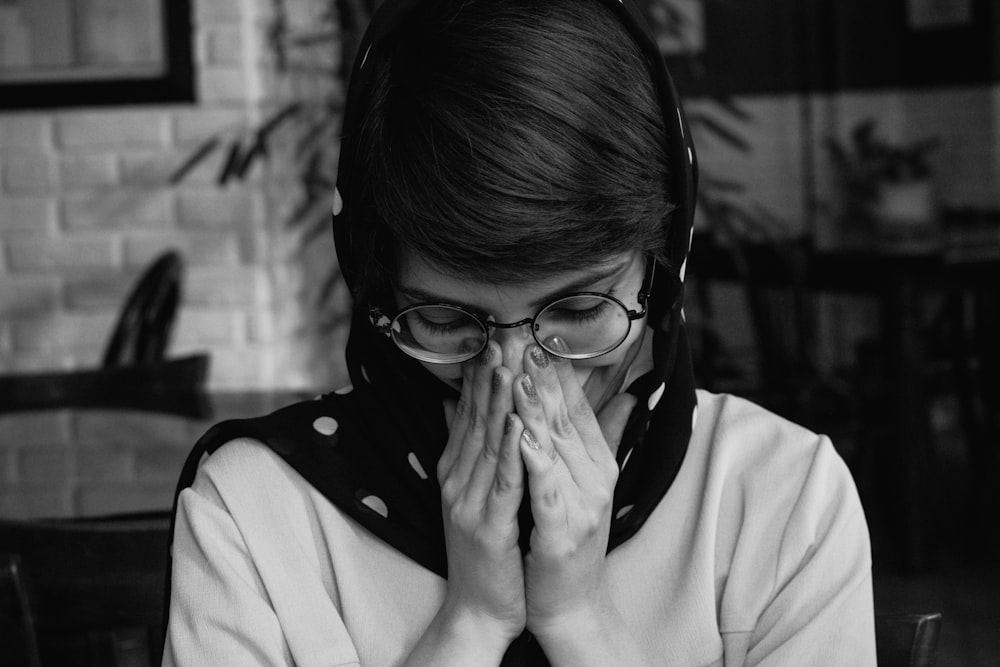 a woman wearing glasses covers her face with her hands