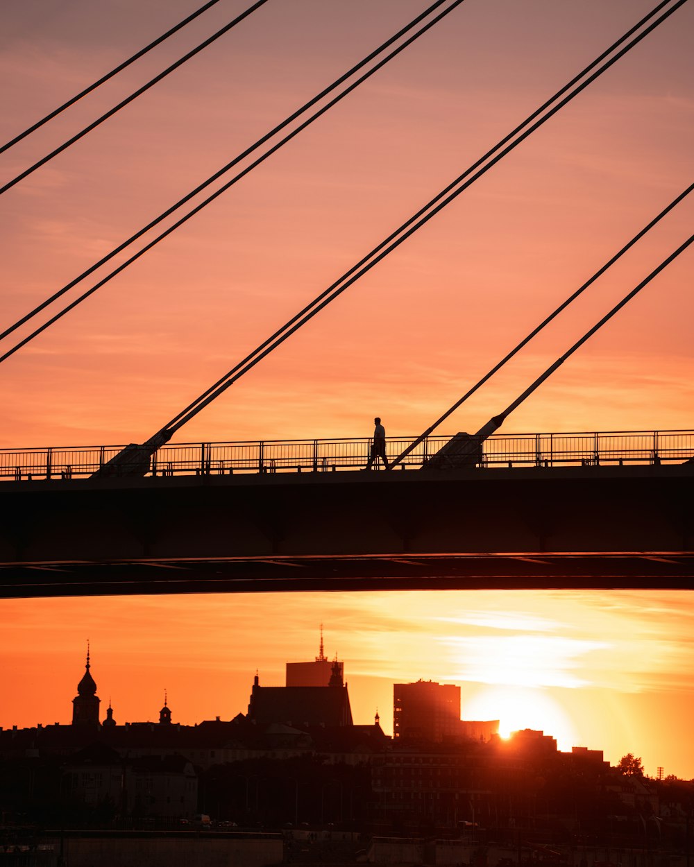 a person walking across a bridge at sunset