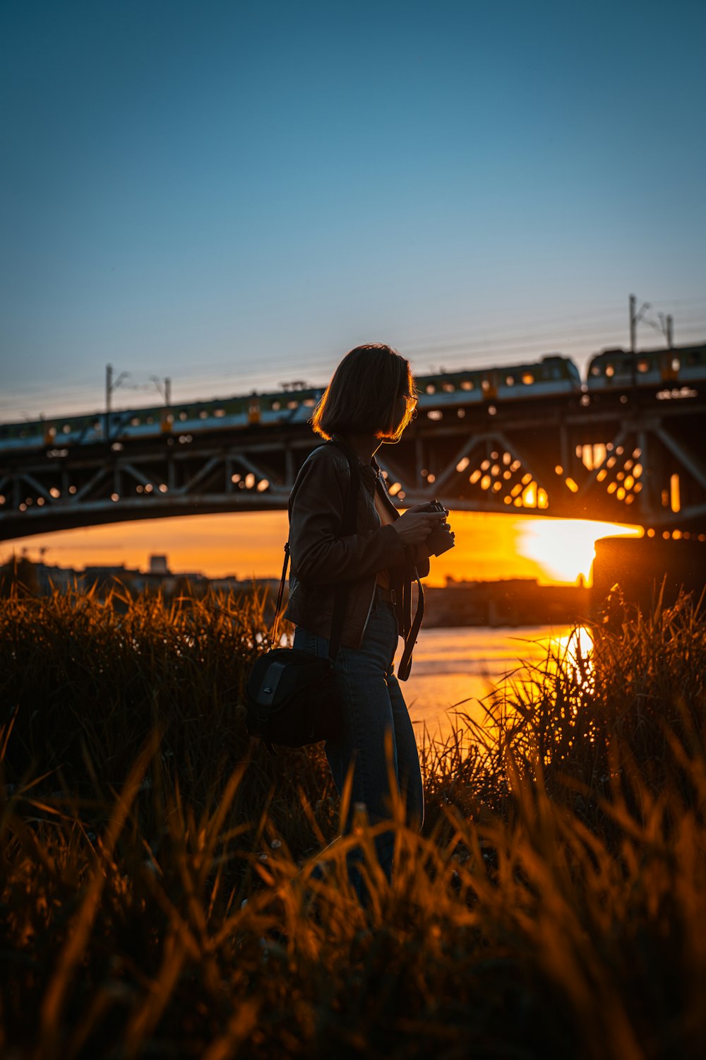 a woman taking a picture of a bridge at sunset