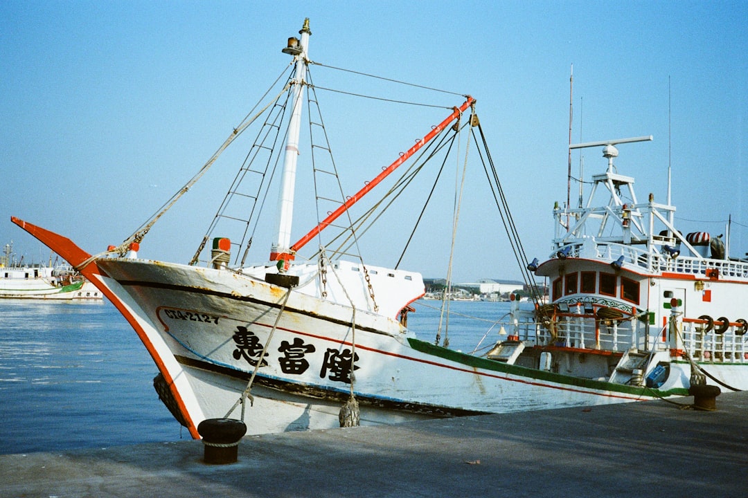 A watercolor painting of a bustling fishing harbor in Taiwan, with colorful fishing boats docked, fishermen at work, and distant mountains under a bright spring sky.