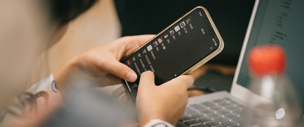 a person using a cell phone while sitting in front of a laptop