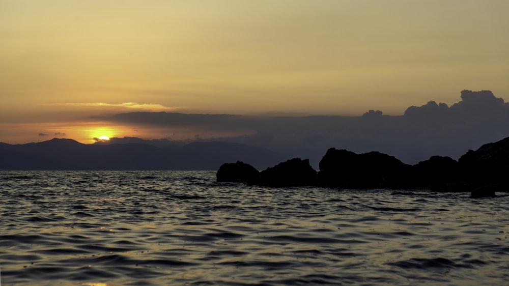 the sun is setting over the ocean with rocks in the foreground