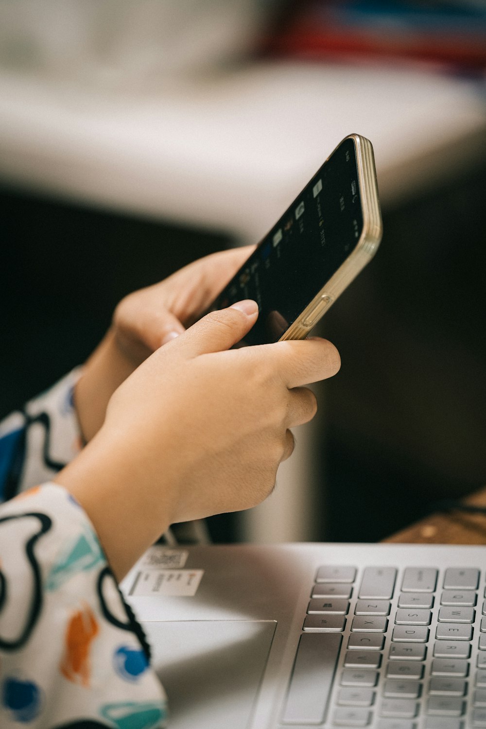 Eine Person, die ein Mobiltelefon benutzt, während sie vor einem Laptop sitzt