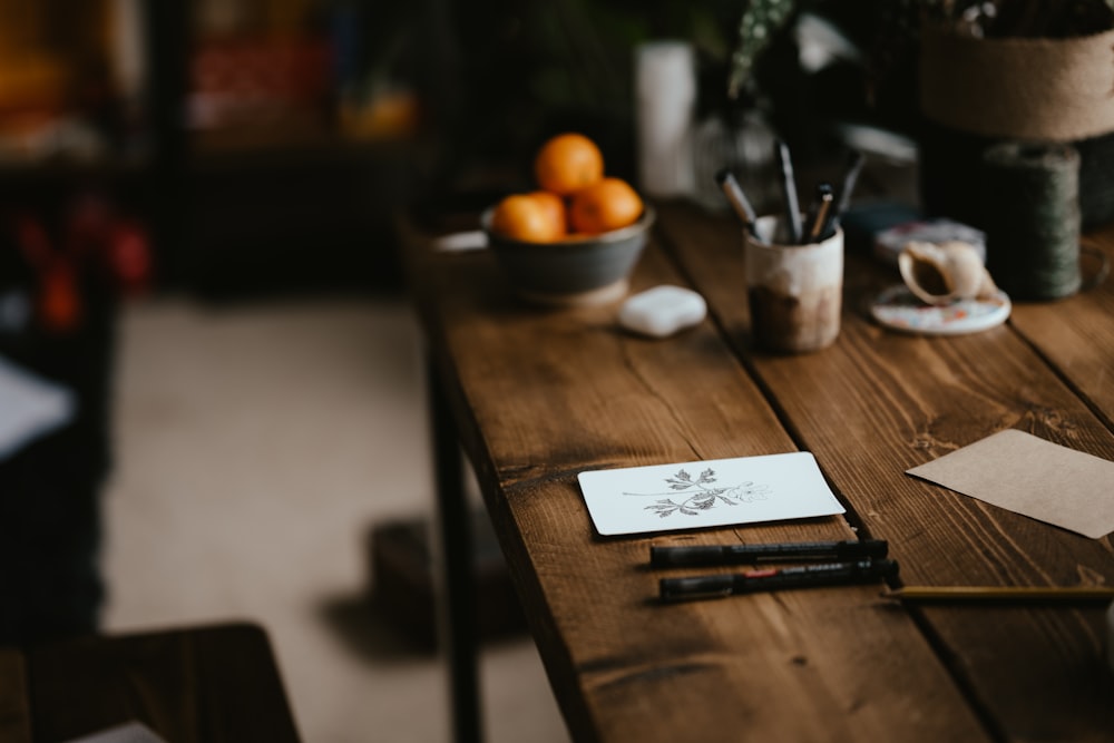 a wooden table topped with a notepad next to a bowl of oranges