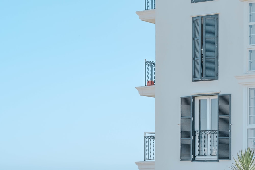 a tall white building with black shutters and balconies