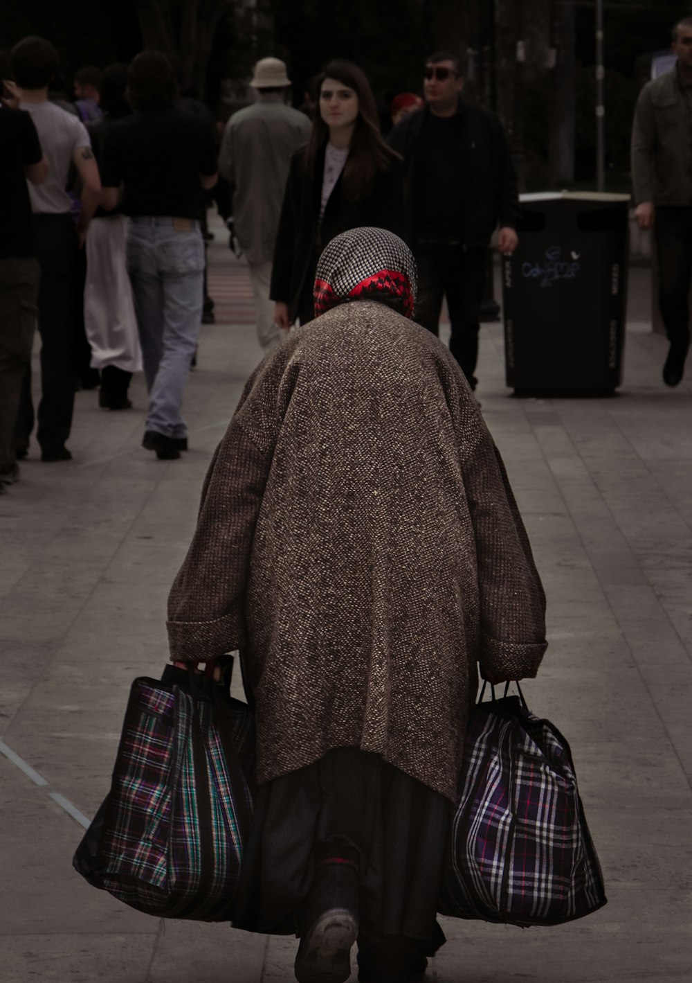 a woman walking down a sidewalk carrying bags of luggage