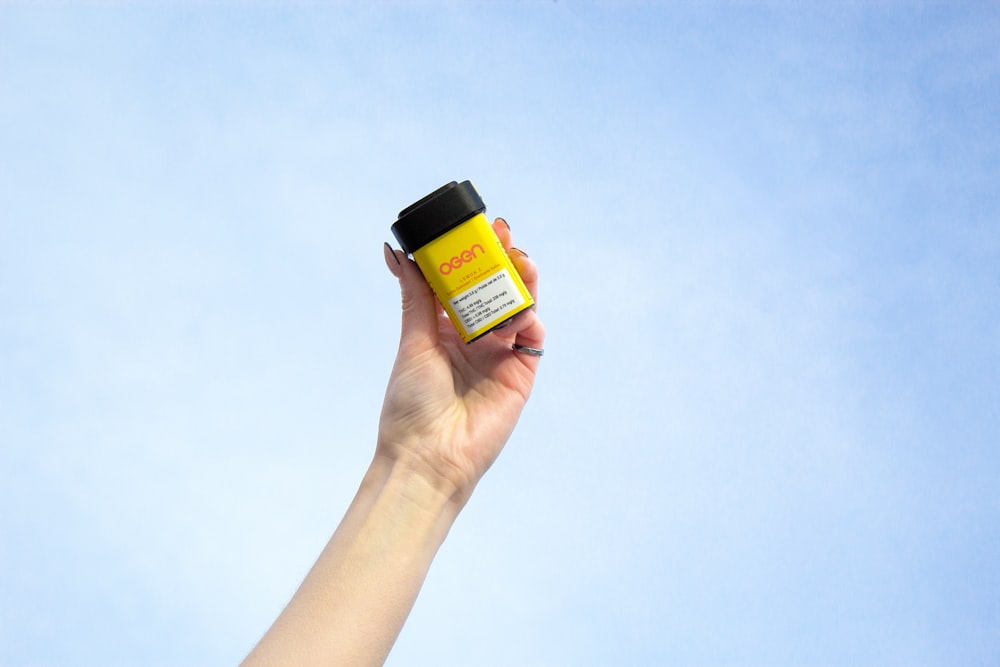 a hand holding a jar of sunscreen against a blue sky