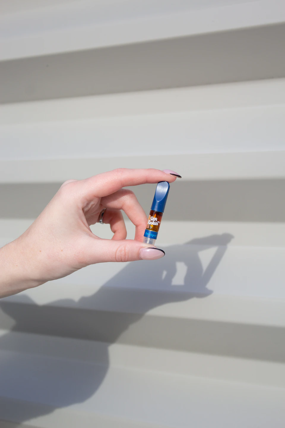 Person's hand holds small blue and gold device with fingers curled around it