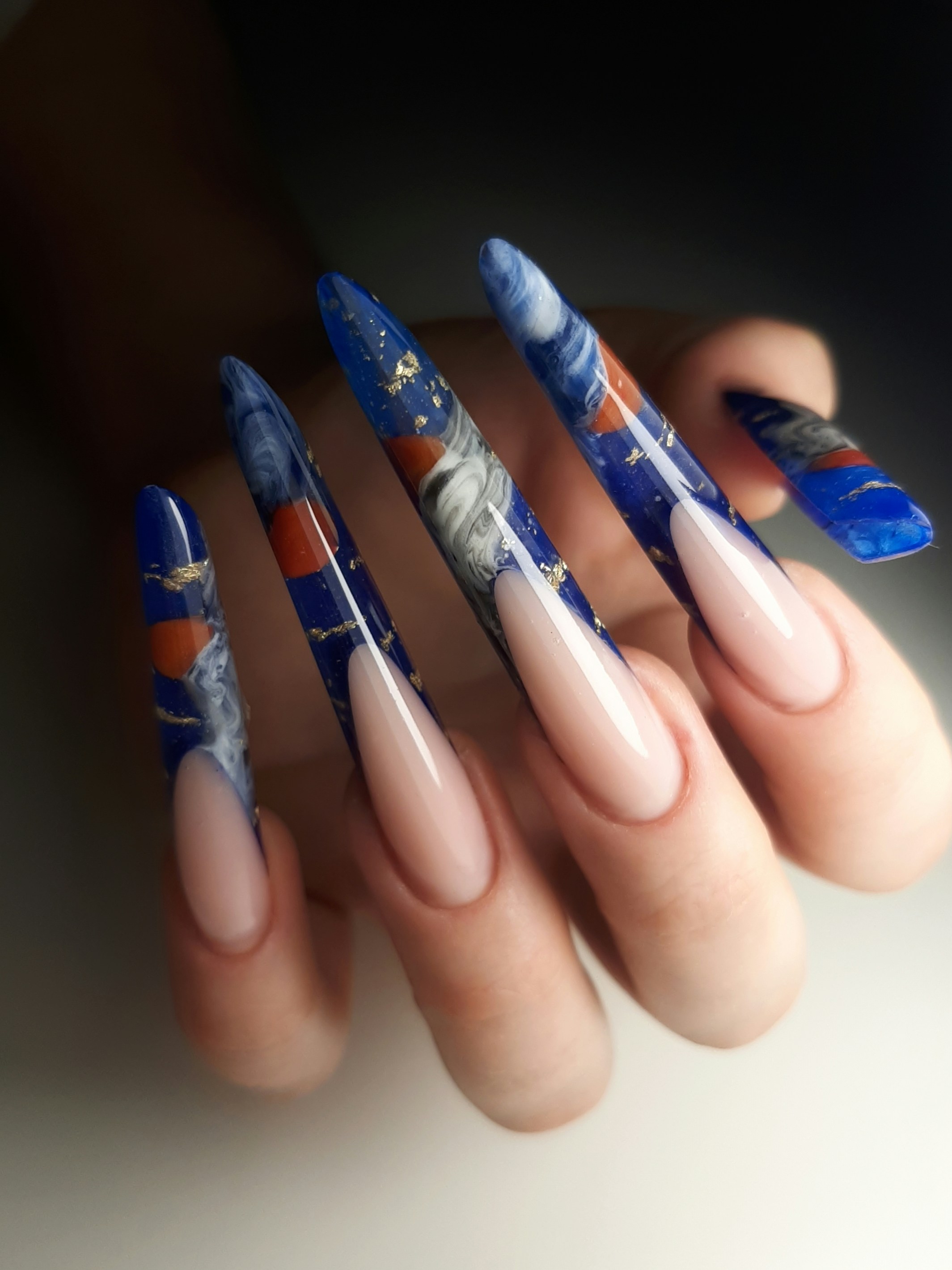 Bold red stiletto nails with hand-painted floral detail and gold foil accents, dramatic lighting