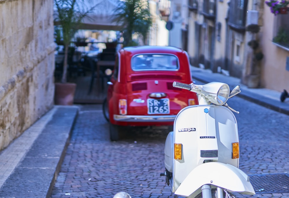 a scooter parked on the side of a street next to a red car