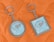 Two keychains lie on an orange quilted fabric background. One keychain is circular, while the other is square. Both have a metallic frame and feature a design with text that reads 'We are exporter of export quality bed sheets' surrounding an image of sheets.