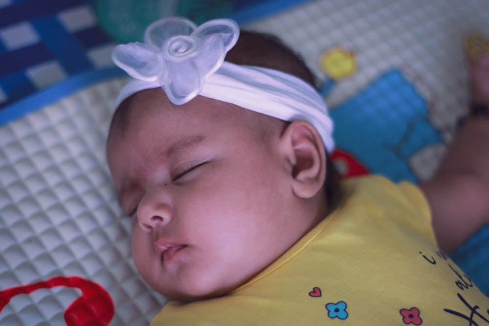 a baby with a white bow laying on a bed