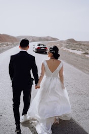 a bride and groom walking down the road holding hands