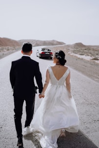 a bride and groom walking down the road holding hands