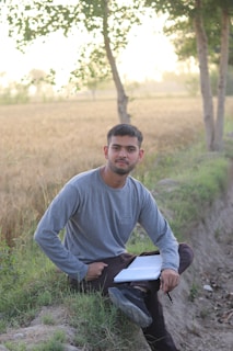 a man sitting in a field with a paper in his lap