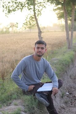 a man sitting in a field with a paper in his lap