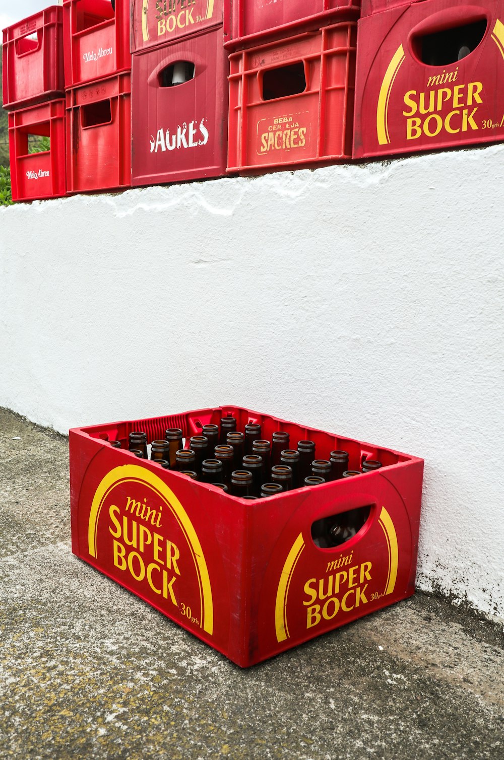 Una scatola rossa piena di bottiglie di birra accanto a un muro bianco