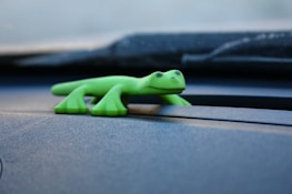 Picture of a GEICO gecko mascot standing beside a car.